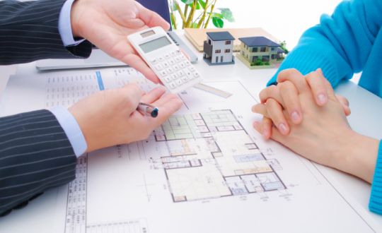 住宅の設計図の上で電卓を持ちお客様へ提案しているビジネスマンの様子
