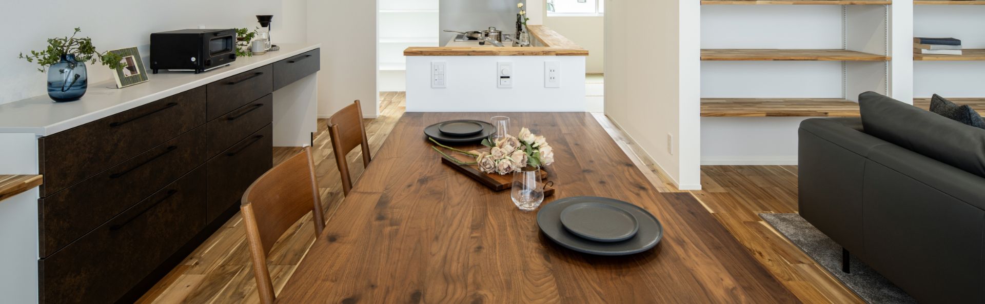 モダンな木目調のダイニングテーブルとキッチン、ソファが配置された開放的なLDKの様子